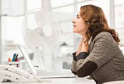 Image of an office worker trying to keep cool using a fan at her desk.